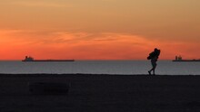 2020:HUNTINGTON BEACH CALIFORNIA.Pretty Orange Sky Ships In Water Near Horizon Line Person Walks Along Beach