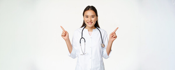 Smiling professional physician in white robe, pointing fingers sideways and showing two advertisements, both ways, standing against white background