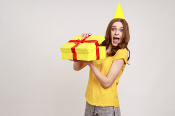 Poster - Portrait of excited amazed brown haired young woman unpacking gift box with surprised expression, enjoying unwrapping birthday present. Indoor studio shot isolated on gray background.