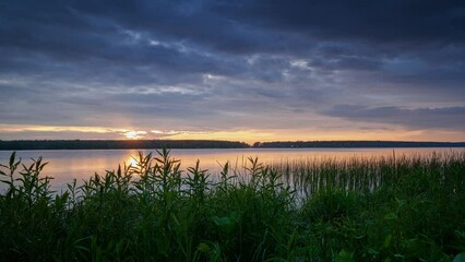 Wall Mural - Sunset with clouds over the river, green grass