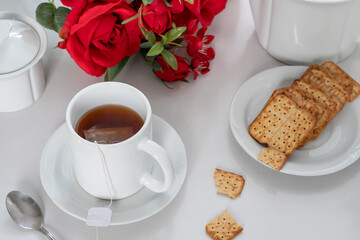 Wall Mural - cup with tea on a table, cookies on a plate, bouquet of red roses