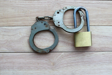 Metal padlock tied to rusty steel handcuffs isolated on wooden background closeup.