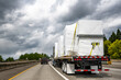 Powerful big rig semi truck tractor transporting heavy duty equipment on flatbed semi trailer driving on the multiline highway road with storm sky
