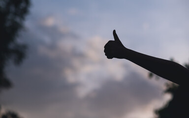 Wall Mural - Silhouette of people making and showing thumbs up hand sign with blurred sunset sky background