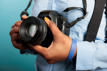 Wall Mural - Close up of african american young adult woman having modern DSLR device while standing on blue background. Professional photographer with photo camera getting ready for shooting session.