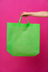 Wall Mural - Female hand holding eco or reusable shopping bag against pink background