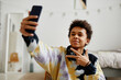 © Seventyfour - Portrait of smiling black teenager with smartphone filming video for social media at home