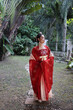 Young attractive Asian woman wearing tadeonal Chinese red hanfu long skirt dress costume scarf hairpin earing outdoor green garden