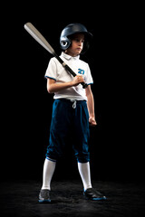 Full-length portrait of kid, beginner baseball player in sports uniform posing with baseball bat isolated on dark background. Concept of sport, achievements, competition