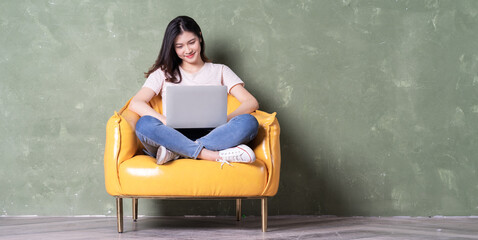 Wall Mural - Image of beautiful young Asian woman sitting on yellow armchair