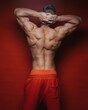 Muscular male back with hands behind head. Athletic young guy shows his strong muscles on his back. Back of bodybuilder on red background in studio. Hands behind mans head.