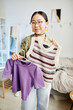 © Seventyfour - Vertical portrait of Asian teenage girl trying on different tops for trendy outfit