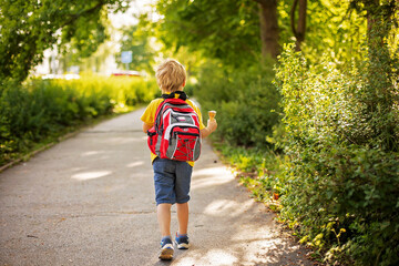 Wall Mural - Adorable kid in colorful clothes and backpack, walking away and eating ice cream on a sunny summer afternoon, warm day