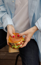 The Girl Is Holding A Juicy Cheeseburger In Her Hand. A Delicious Burger In A Woman’s Hands Close Up. A Perfect Hearty Dinner. A Girl Is Ready To Eat A Burger