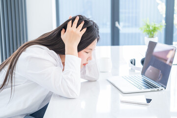 Young asian tired business woman with long hair working at laptop in bright home office