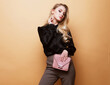 © Raisa Kanareva - Beautiful blond woman in a blouse and pants holding handbag posing over beige background.
