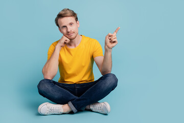 Wall Mural - Reliable guy sit floor hand cheek direct finger empty space wear casual clothes isolated on turquoise background