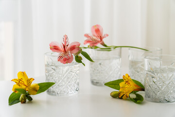 Sticker - yellow and pink alstroemeria flowers near glasses with water on white tabletop.