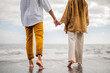 canvas print picture - Young loving couple shown from behind holding hands on a beach