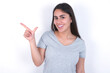 © Roquillo - Young beautiful brunette woman wearing gray T-shirt over white wall pointing up with fingers number eight in Chinese sign language BÄ.