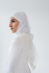 Wall Mural - young muslim woman in hijab and wedding dress looking away isolated on grey.