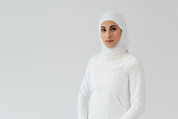 Wall Mural - portrait of muslim bride in white hijab and wedding dress looking at camera isolated on grey.