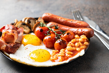 English breakfast with fried eggs, sausages, bacon, beans, mushrooms, toasts on white plate at the restaurant. Close up of detail