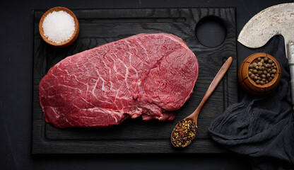 Wall Mural - Raw beef tenderloin lies on a wooden cutting board on a black table, top view