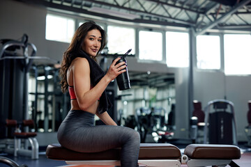 Wall Mural - Young active woman taking a break in the gym and drinking protein shake.