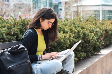 Wall Mural - Young girl student sitting on street bench using laptop computer