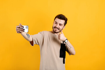 Wall Mural - Handsome young man wearing casual clothes posing isolated over yellow background doing okay gesture while taking selfie or having video call.