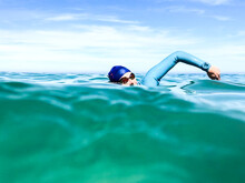 Swimmers Upper Body Seen From Water Level Doing Freestyle Stroke Wearing Wetsuit, Cap And Goggles