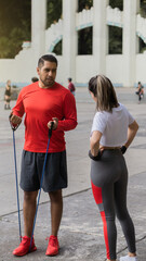 Wall Mural - Handsome Latino trainer teaching resistance exercise routine to an unrecognizable woman.