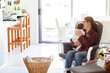 © Austockphoto - Young mum in fourth trimester singing newborn baby to sleep on rocking chair in messy house