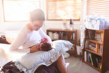 Young Mum In Bedroom Breastfeeding Content Newborn Baby With Light Flare