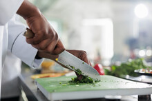 Close Up Of African American Hands Using Professional Knife To Chop Finely Fresh Organic Herbs And Vegetables For Stew Recipe. Cook Cutting Greens For Gourmet Dish Served At Fine Dining Restaurant.