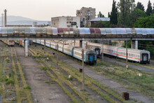Abandoned Passenger Wagons On Railroad Tracks Overgrown With Grass Under The Bridge. Decommissioned Trains. Tbilisi, Georgia. 