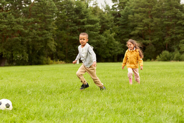 Wall Mural - childhood, leisure games and people concept - happy little boy and girl with ball playing soccer at summer park