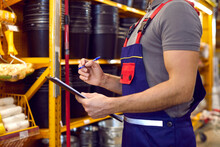 Inventory And Check Availability Of Goods In Warehouse Of Building Materials Store. Close Up Of Clipboard In Hands Of Young Male Worker In Overalls Who Writes Information. Cropped Image.