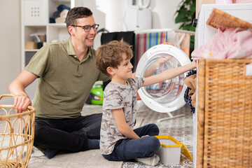 Wall Mural - Man spends time with young child in laundry room, bathroom, performs household duties on paternity leave, takes care of son, boy helps put clothes in drum.