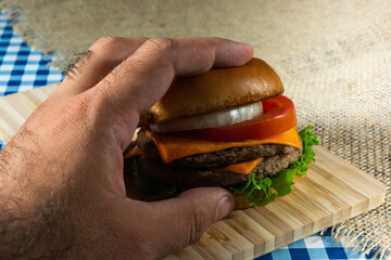 male hand picking up a double meat salad cheeseburger, top view.