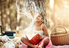 Open A Book And You Open Your Mind. Shot Of A Little Girl Reading A Book With Her Toys In The Woods.