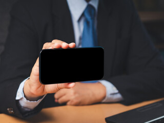 Wall Mural - businessman in a suit holding a blank screen smartphone while sitting in the office