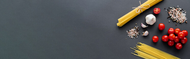 Canvas Print - Top view of raw spaghetti near garlic and spices on black surface with copy space, banner.