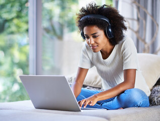 Poster - Whiling away the day online. Shot of a young woman sitting at home using a laptop and wearing headphones.