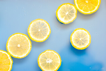 Wall Mural - Lemon slices in water on blue background. Swimming lemon slices background.