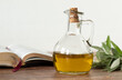 Pure olive oil in a glass jar, an open Bible Book, and a green olive branch on a wooden table with white background. Symbol of God's Holy Spirit. Christian biblical concept. Copy space. A close-up.