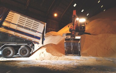 Wall Mural - Excavator, Backhoe unloading raw brown sugar inside huge warehouse. Bulk sugar handling, and transportation.