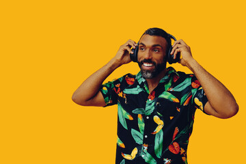 handsome mid adult bearded african american man with headphones listening music posing on yellow background looking away at copy space studio shot