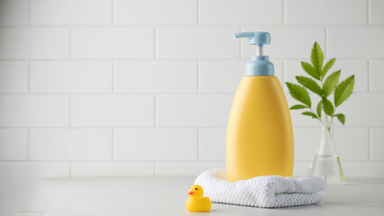 Yellow bottle of children cosmetic product and toy rubber duck in bathroom. Copy space